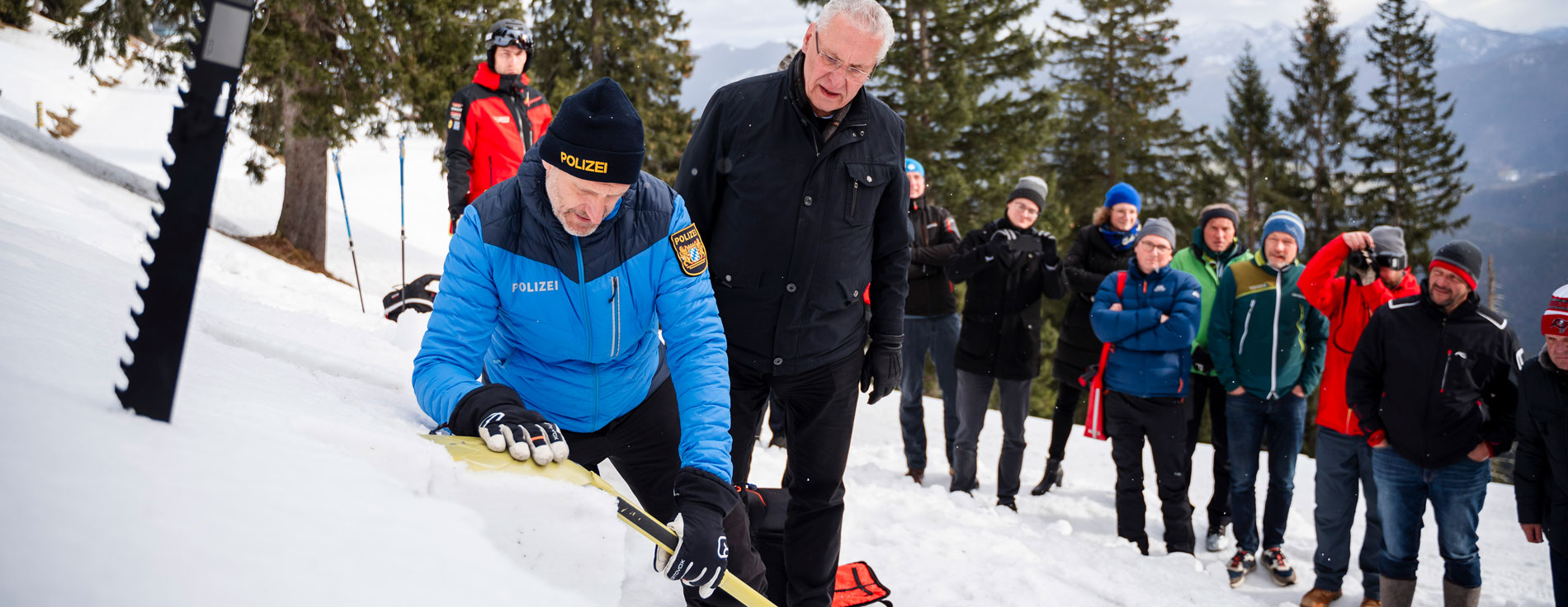 Gute Vorbereitung, Vorsicht, Rücksicht und Respekt: Innenminister Joachim Herrmann und das Kuratorium für Alpine Sicherheit informieren zur Unfallprävention in den Bergen. Innenminister Herrmann und Einsatzkräfte, u.a. ein Polizist, mit Lawinenschaufeln im Schnee