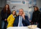 Innenminister Joachim Herrmann mit Telefonhörer am Ohr, im Hintergrund Kinder auf Kinderpolizeiwache