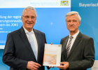 Innenminister Joachim Herrmann und Dr. Thomas Gößl mit Broschüre in der Hand, im Hintergrund Präsentation
