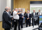 Herrmann im Gespräch mit einer Person, viele weitere stehen dabei, rechts moderne Bildschirme