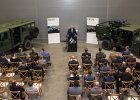 Herrmann am Rednerpult zwischen olivgrünen Panzerfahrzeugen