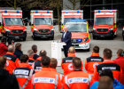 Herrmann am Rednerpult vor Rettungswägen, im Vordergrund Rettungskräfte in Uniform von hinten