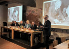 Innenminister Joachim Herrmann und Vertreter der Vorstandschaft an Tischen vorne, im Hintergrund alte Schwarzweiß-Aufnahmen an Leinwand