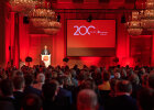Blick über das Publikum zur Bühne in roter festlicher Beleuchtung und Leinwand mit "200 Jahre Sparkasse", Minister Herrmann am Rednerpult