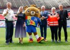 Gruppenfoto mit Vertretern der Sicherheitskräfte, Herrmann und Maskottchen auf Fußballfeld