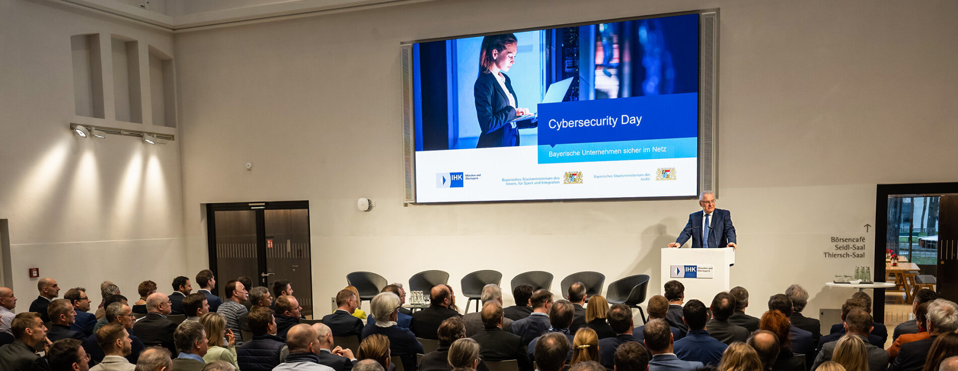 26. Januar 2023: Cybersecurity Day: Gemeinsam mit Justizminister Georg Eisenreich und IHK-Präsident für München und Oberbayern, Prof. Klaus Josef Lutz, hat Innenminister Joachim Herrmann zum Cybersecurity Day in München eingeladen. Herrmann: „Cybersicherheit wird ein immer wichtigerer Wettbewerbsvorteil für die Wirtschafts- und Innovationskraft bayerischer Unternehmen. Denn mit der zunehmenden Vernetzung steigt auch die digitale Verwundbarkeit.“ Bei dem Aktionstag informierten Experten in Vorträgen und Workshops über die aktuelle Bedrohungslage und mögliche Maßnahmen gegen Hacker, Erpresser und Spione. Blick von hinten über Zuschauer zum Rednerpult mit Innenminister Joachim Herrmann