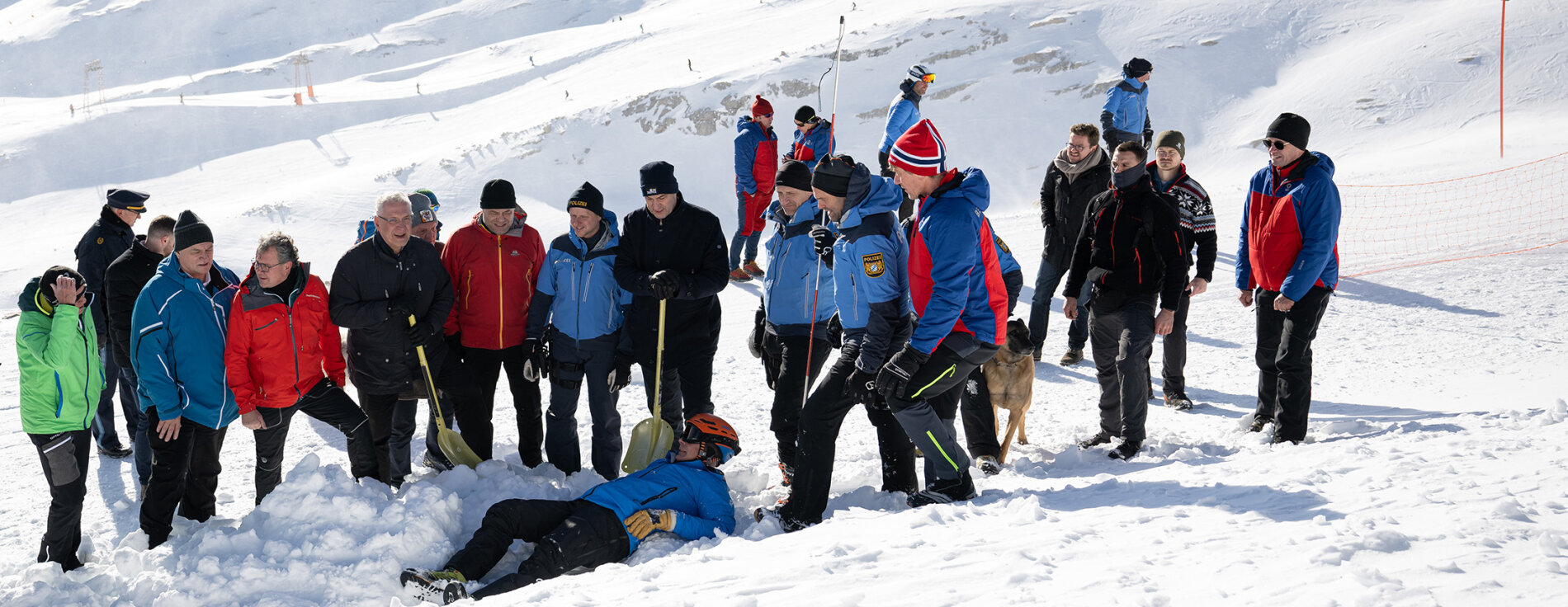 Vorführungen zu Rettungen von Lawinenverschütteten Mehrere Personen stehen mit Schaufeln um eine im Schnee liegende Person herum