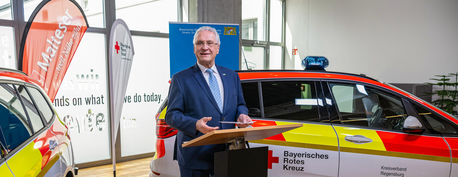 Innenminister Joachim Herrmann am Rednerpult zwischen zwei neuen Rettungseinsatzfahrzeugen