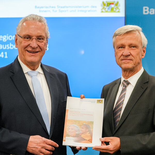 Innenminister Joachim Herrmann und Dr. Thomas Gößl mit Broschüre in der Hand, im Hintergrund Präsentation