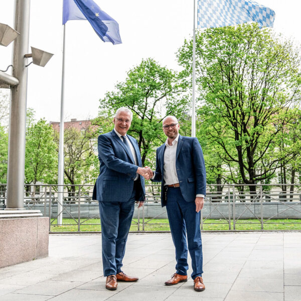 Herrmann und Mehring schütteln sich die Hand vor Fahnenmasten vor Staatskanzlei