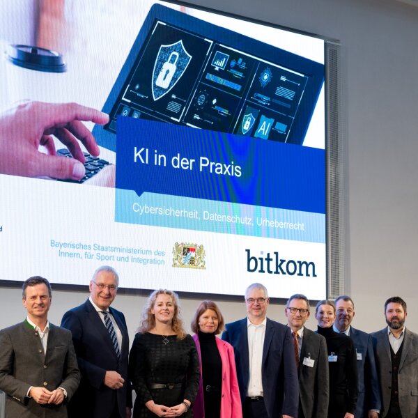 Gruppenfoto vor Präsentationsleinwand "KI in der Praxis" mit Innenminister Herrmann und weitere Akteure der Veranstaltung