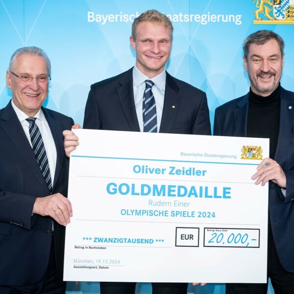 Auf dem Bild sind der Ruder-Olympiasieger Oliver Zeidler sowie Sport- und Innenminister Joachim Herrmann und Ministerpräsident Dr. Markus Söder mit einem Scheck über 20.000 Euro zu sehen.