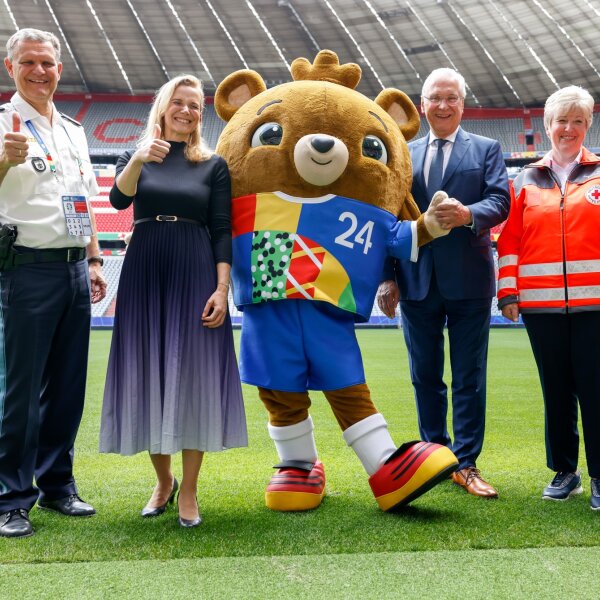 Gruppenfoto mit Vertretern der Sicherheitskräfte, Herrmann und Maskottchen auf Fußballfeld