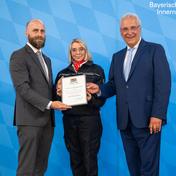 Innenminister Herrmann und zwei geehrte Personen mit Urkunde vom Betrieb AFAG Messe und Ausstellungen GmbH aus Nürnberg