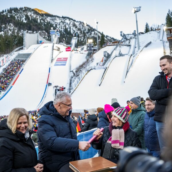 Herrmann übergibt neben Bundesinnenministerin Faeser Stab an die baden-württembergische Kultus-, Jugend- und Sportministerin Theresa Schopper, im Hintergrund Skisprungschanze von Oberstdorf