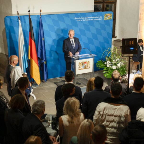 Innen- und Integrationsminister Joachim Herrmann hält auf diesem Bild eine Rede vor einem Publikum bestehend aus Neubürgerinnen und Neubürgern.