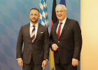 im Bild links  Innenminister Matúš Šutaj Eštok, rechts im Bild Innenminister Joachim Herrmann, biede stehen vor einem Fahnenset 