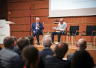 Minister Herrmann bei der Podiumsdiskussion mit Moderator sitzend auf der Bühne