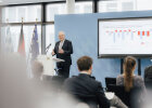 Minister Herrmann am Rednerpult im Hintergrund die Präsentation der Statistik