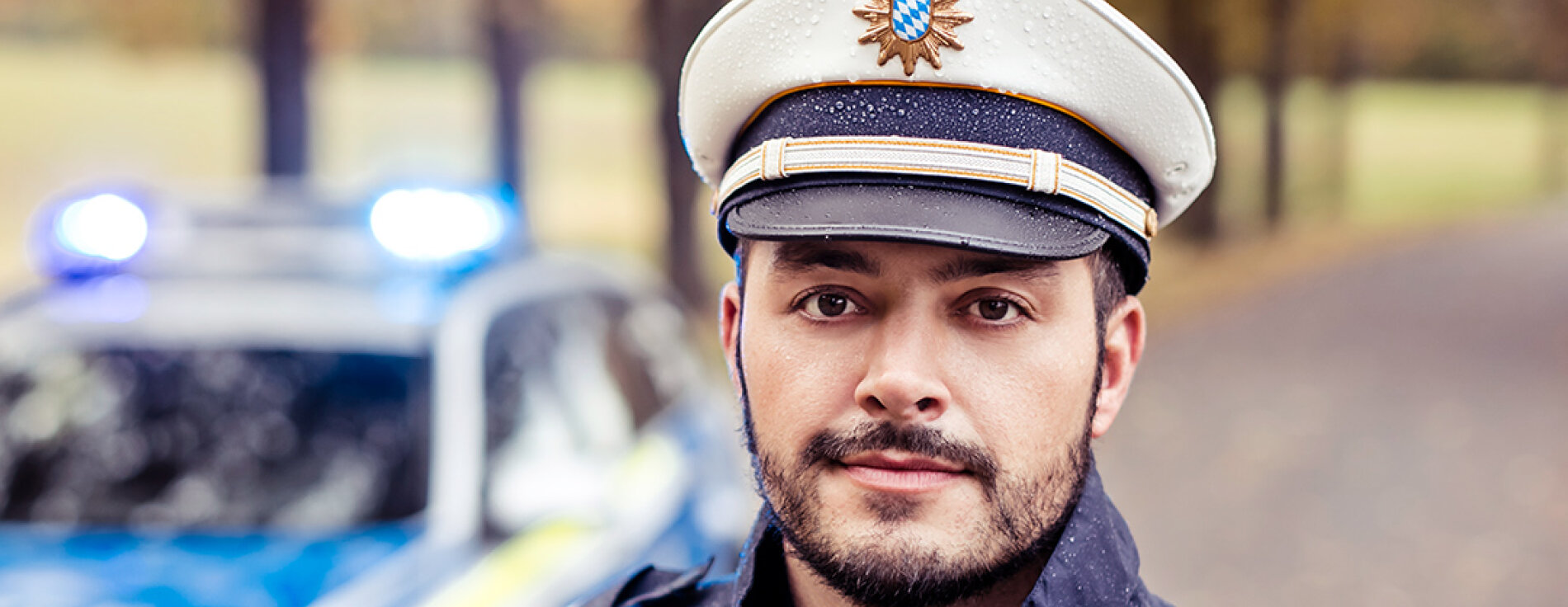 Polizist (m/w/d) Polizist in Uniform vor Streifenwagen