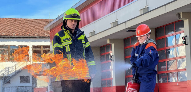 Mit dem Feuerlöscher ein echtes Feuer bezwingen, mit der Rettungsschere Fahrzeuge aufschneiden oder den Atemschutz-Parcours meistern und das in echter Ausrüstung – schnell sind die Schülerinnen und Schüler mit Begeisterung dabei. - © Thomas Kapfer/FF Penzberg Feuerwehrmann und Kind bei Feuerlöschübung