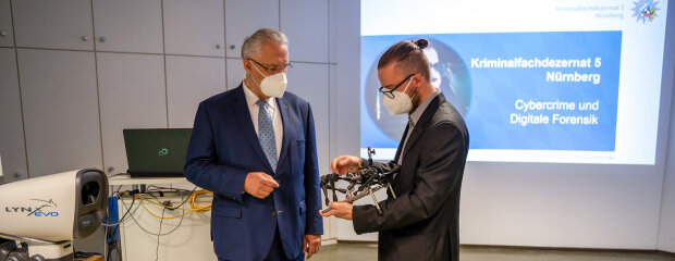 9. Juli 2021: Fortschritt bei der Cybercrime-Bekämpfung: Innenminister Joachim Herrmann hat heute beim Polizeipräsidium Mittelfranken das neue Kriminalfachdezernat 5 ‚Cybercrime und Digitale Forensik‘ (KFD 5) vorgestellt. „Straftäter verlagern ihre kriminellen Machenschaften immer mehr in den digitalen Raum“, erläuterte Herrmann. „Diesem besorgniserregenden Trend setzen wir hochqualifizierte Spezialermittler und IT-Spezialisten sowie eine High Tech-Polizeiausstattung entgegen.“ Innenminister Joachim Herrmann und Spezialist, der technisches Gerät präsentiert