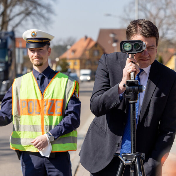Staatssekretär Sandro Kirchner mit Blick durch Blitzgerät, daneben Polizist mit Polizeikelle
