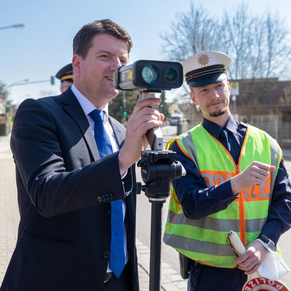 Staatssekretär Sandro Kirchner mit Blick durch Blitzgerät, daneben Polizist