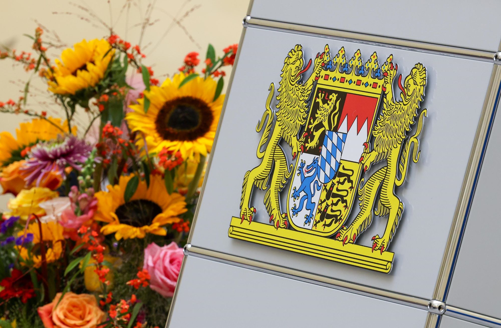 Bayerisches Staatswappen aus Metall neben Blumen