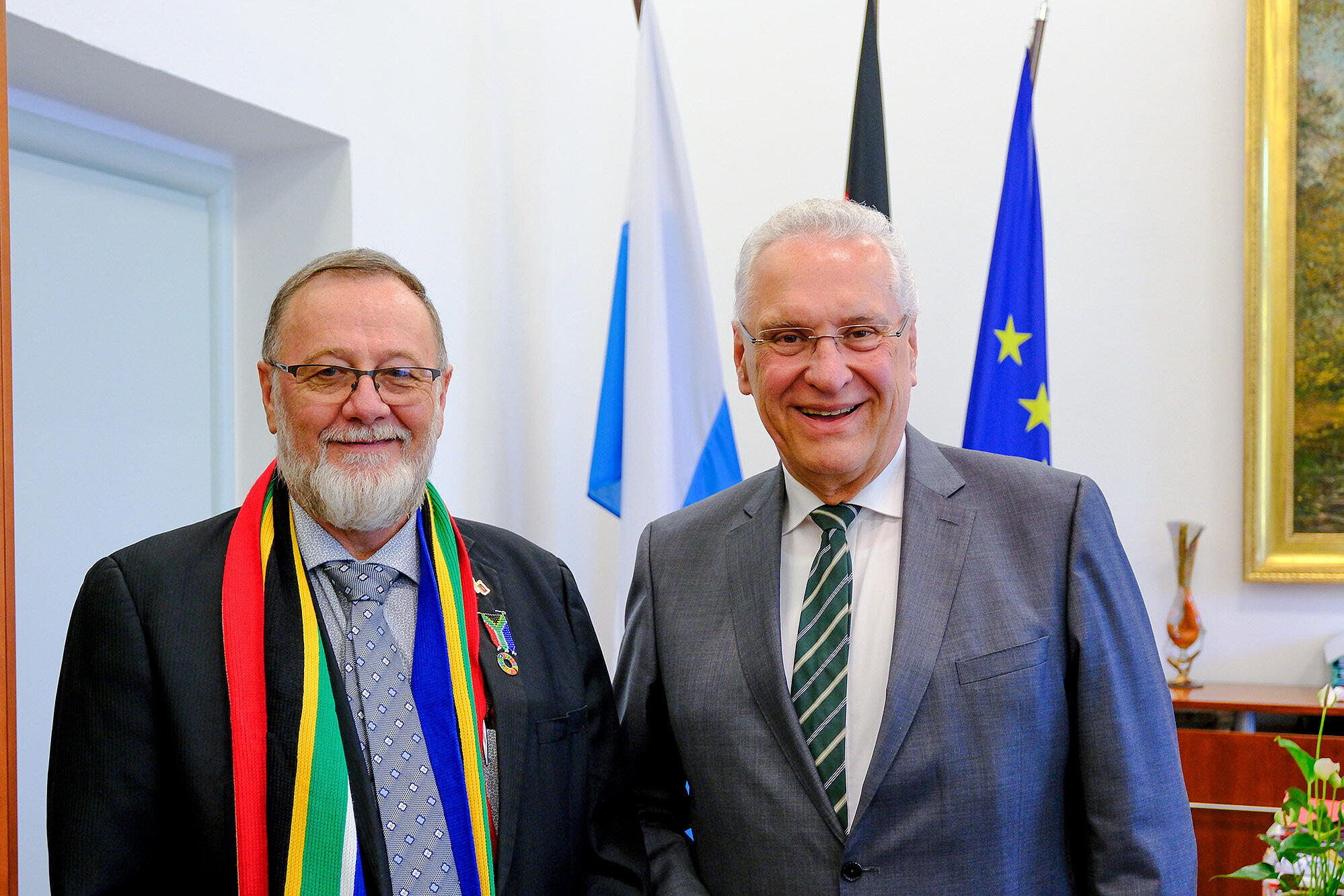 Auf dem Bild links Minister Anton Bredell, rechts Innenminister Joachim Herrmann vor Fahnenset in Büro.