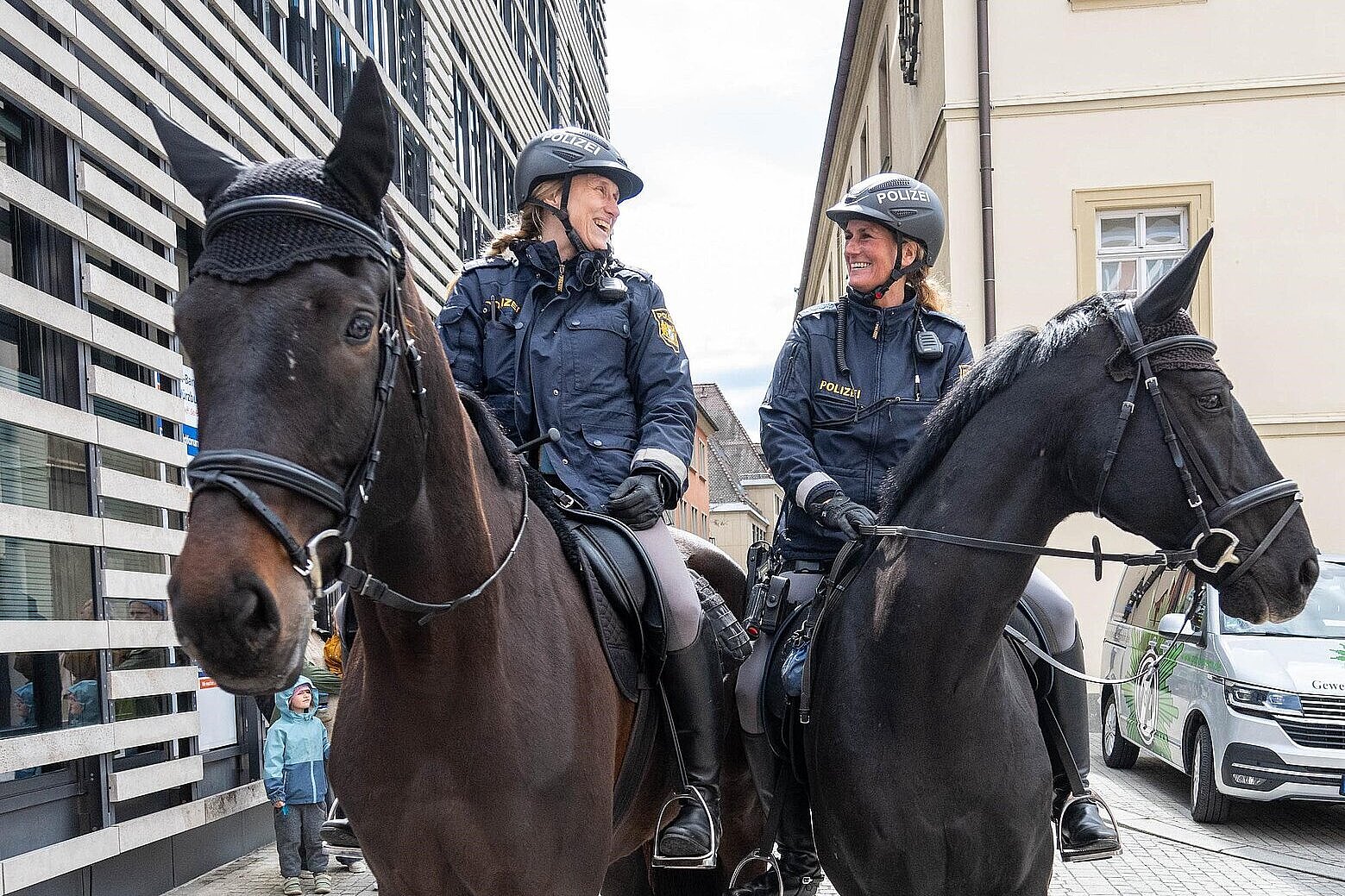Zwei Polizeipferde mit lachenden Polizeireitern in der Stadt unterwegs