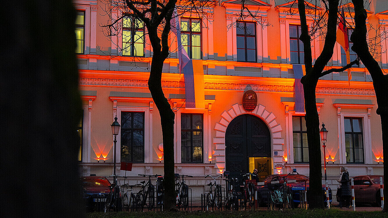 Bayerisches Innenministerium, davor stehen mehrere Fahrräder und ein paar parkende Autos. Im Vordergrund sind kahle Bäume und eine Wiese zu sehen, die Szene wirkt wie am frühen Abend.