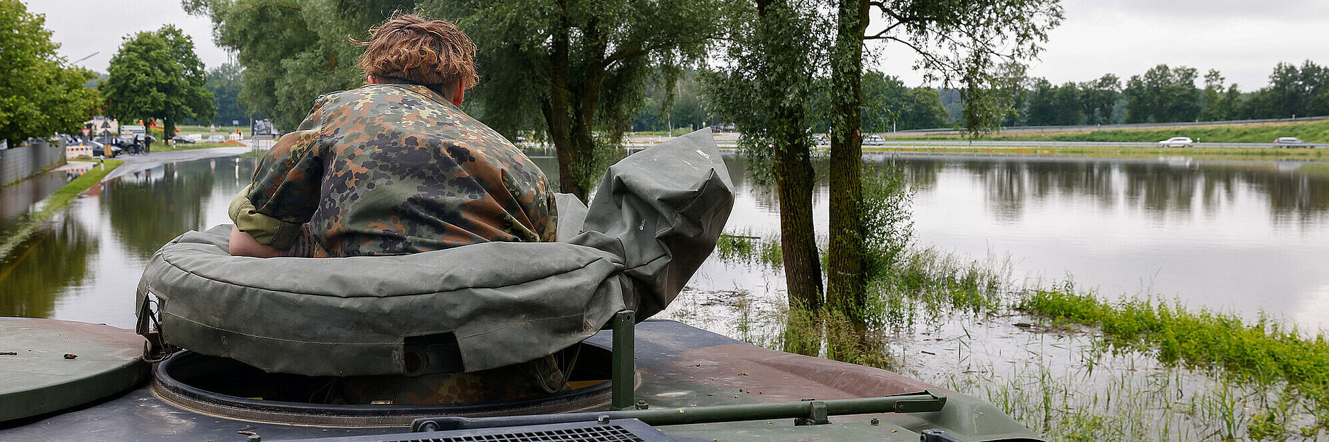 Ein Soldat in Tarnkleidung schaut aus einer Luke auf dem Dach eines Armeefahrzeugs auf überschwemmtes Gebiet