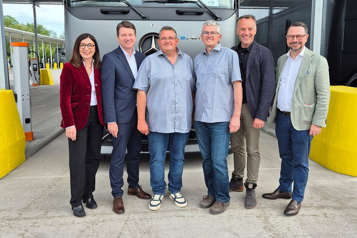 Gruppenbild von links Barbara Becker, MdL Sandro Kirchner, Staatssekretär, Vertreter der Fa. W&P vor einem LKW stehend links und rechst stehen Ladesäulen