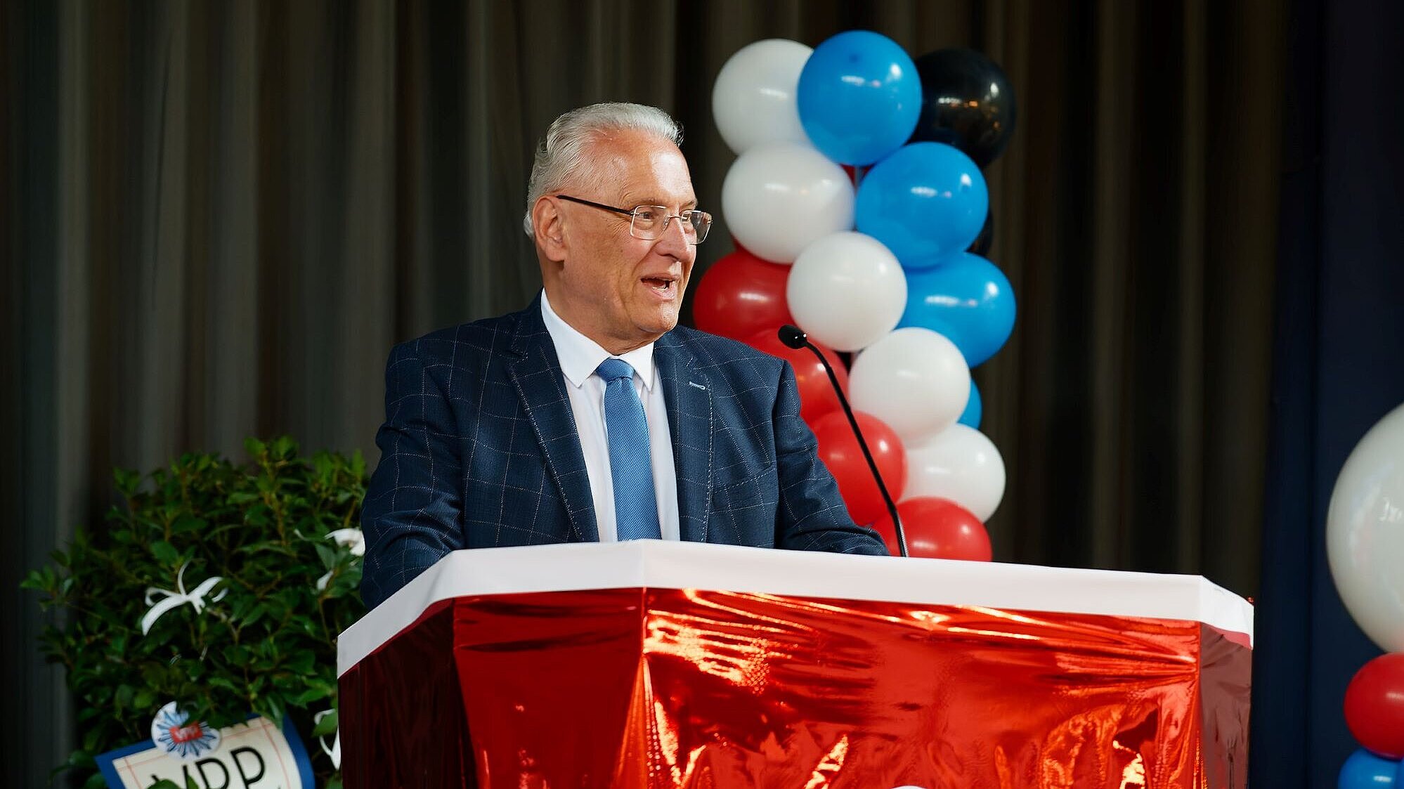 Innenminister Joachim Herrmann am Rednerpult, hinter im bunte Luftballons anlässlich der Feierlichkeiten zum 75. Geburtstag der VPP