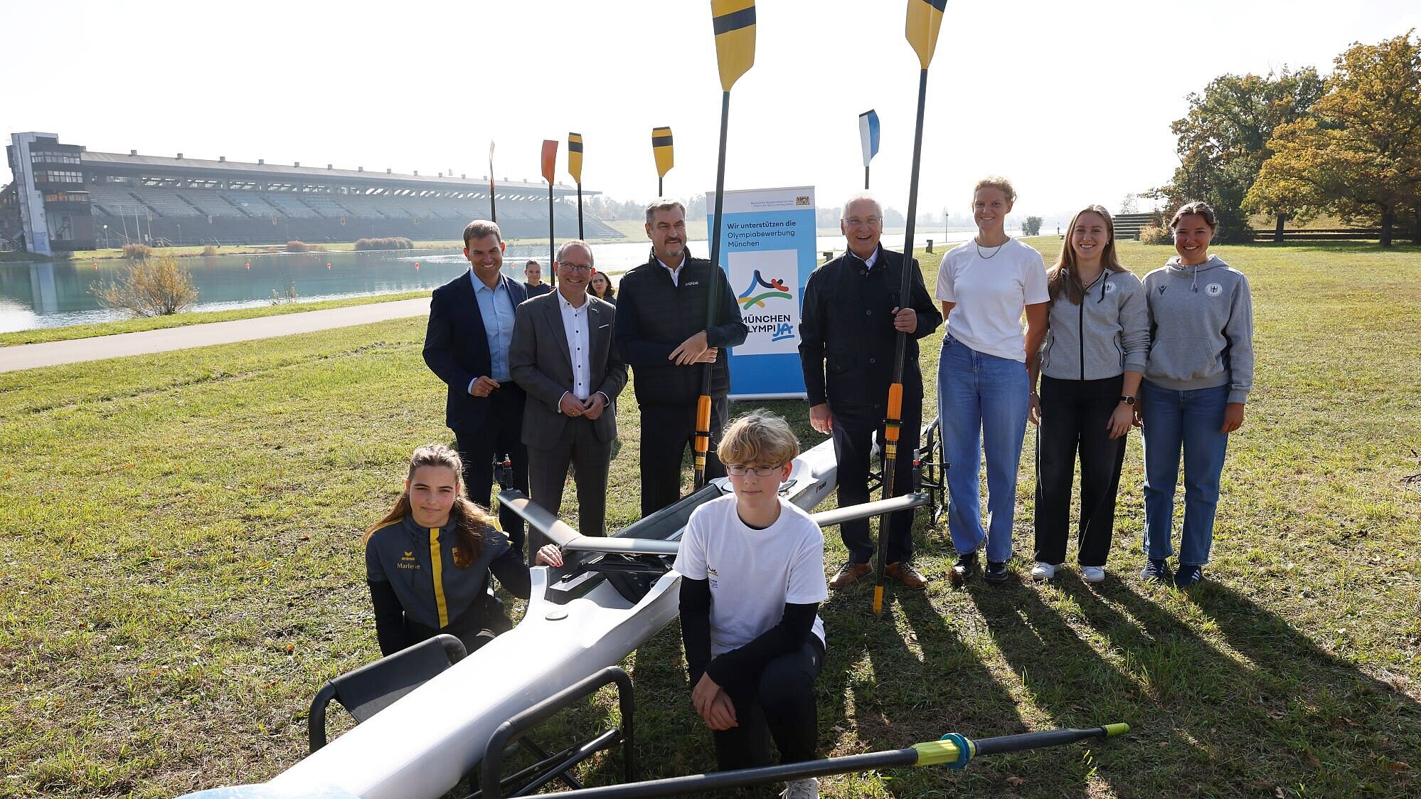 Auf dem Bild sind u.a. Ministerpräsident Dr. Markus Söder und Sportminister Joachim Herrmann mit weiteren Ehrengästen und Rudersportlerinnen und -sportlern vor Rudersportgeräten zu sehen.
