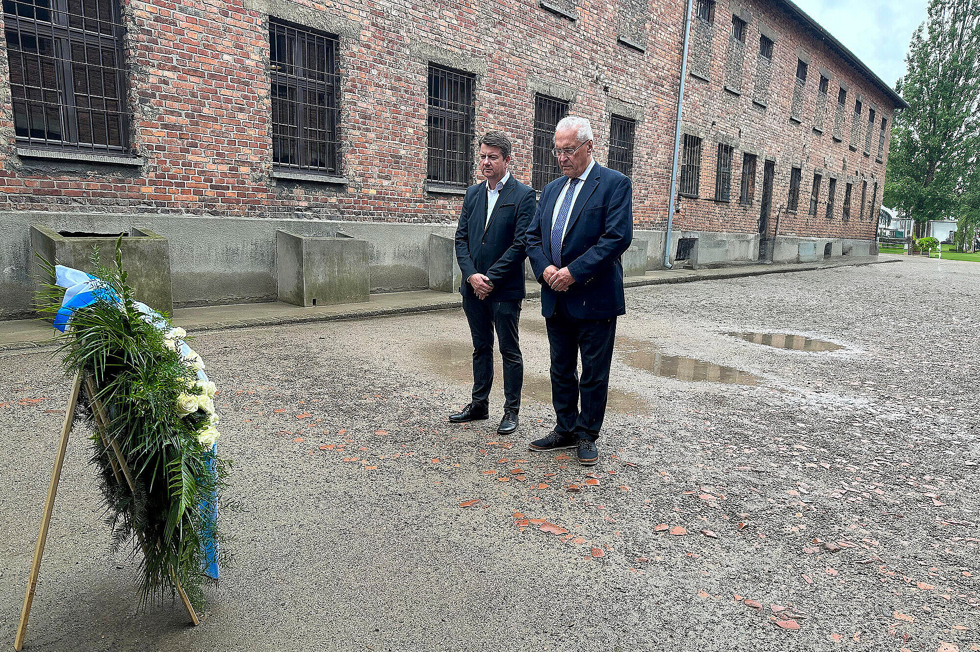 Innenstaatssekretaer Sandro Kirchner links, Innenminister Joachim Herrmann rechts legen einen Trauerkranz in der KZ Gedenkstätte Auschwitz nieder und verweilen davor