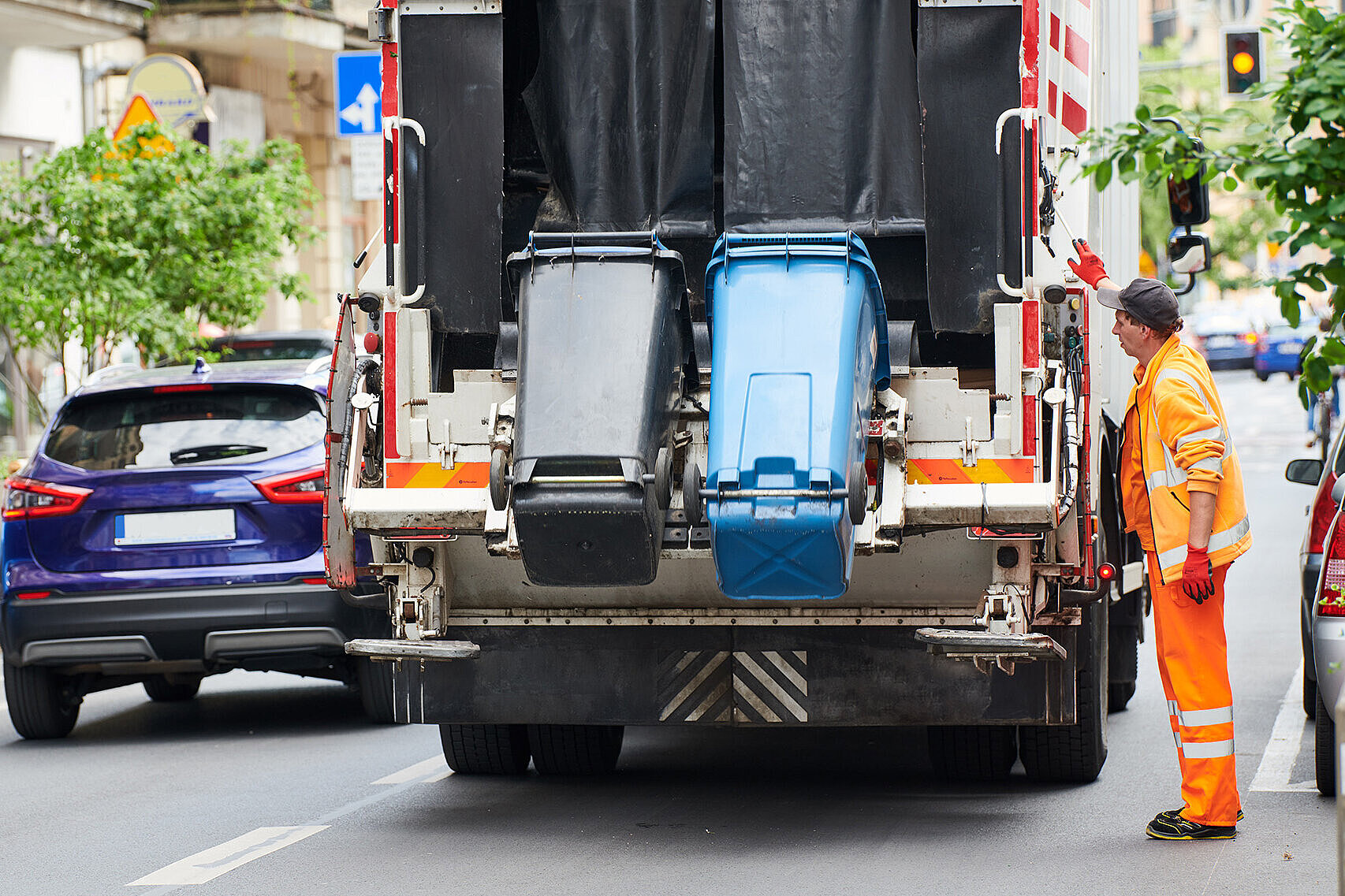Müllmann lädt eine blaue und eine schwarze Mülltonne in den Müllwagen