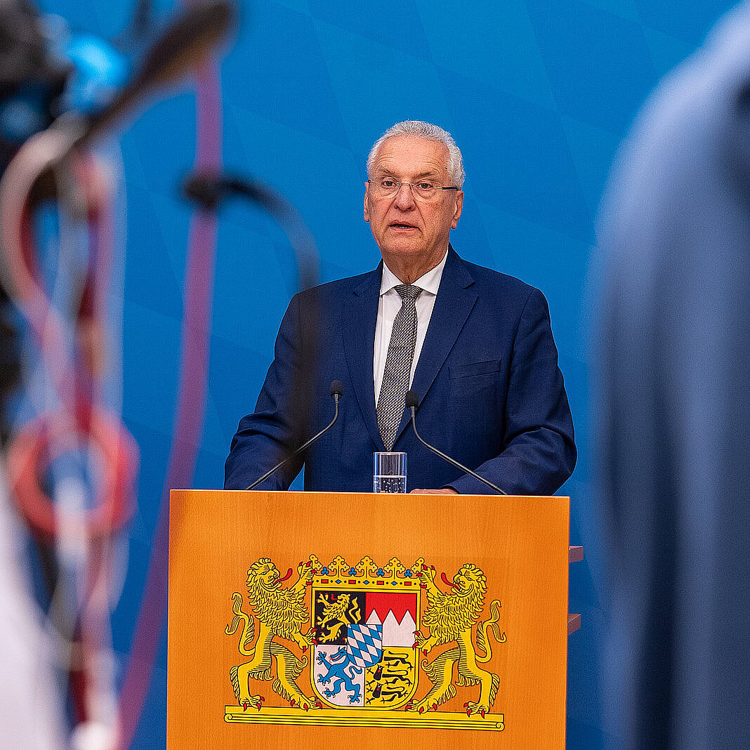 Innenminister Herrmann am Rednerpult, im Vordergrund angeschnittene Person mit Kamera