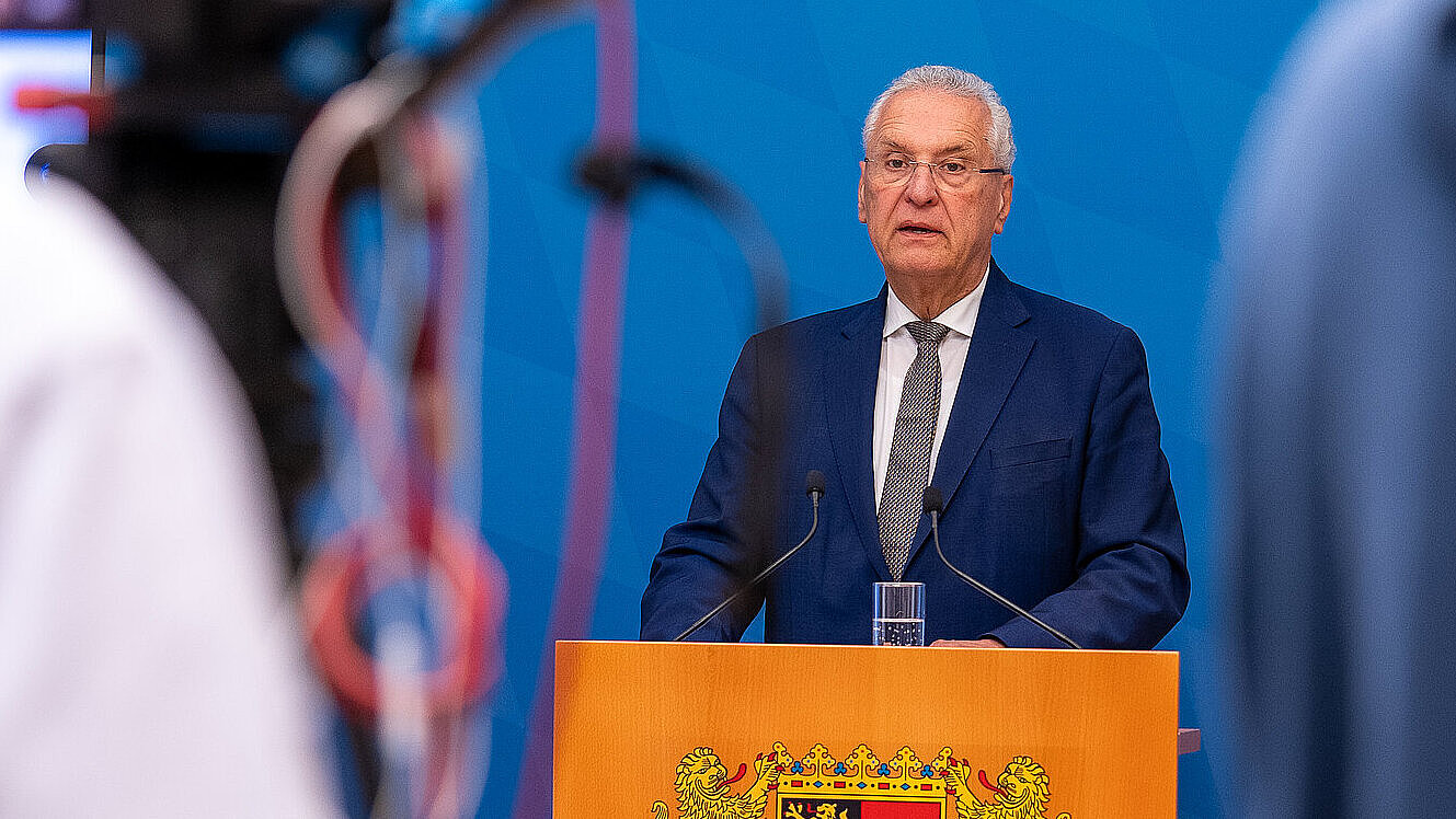 Innenminister Herrmann am Rednerpult, im Vordergrund angeschnittene Person mit Kamera
