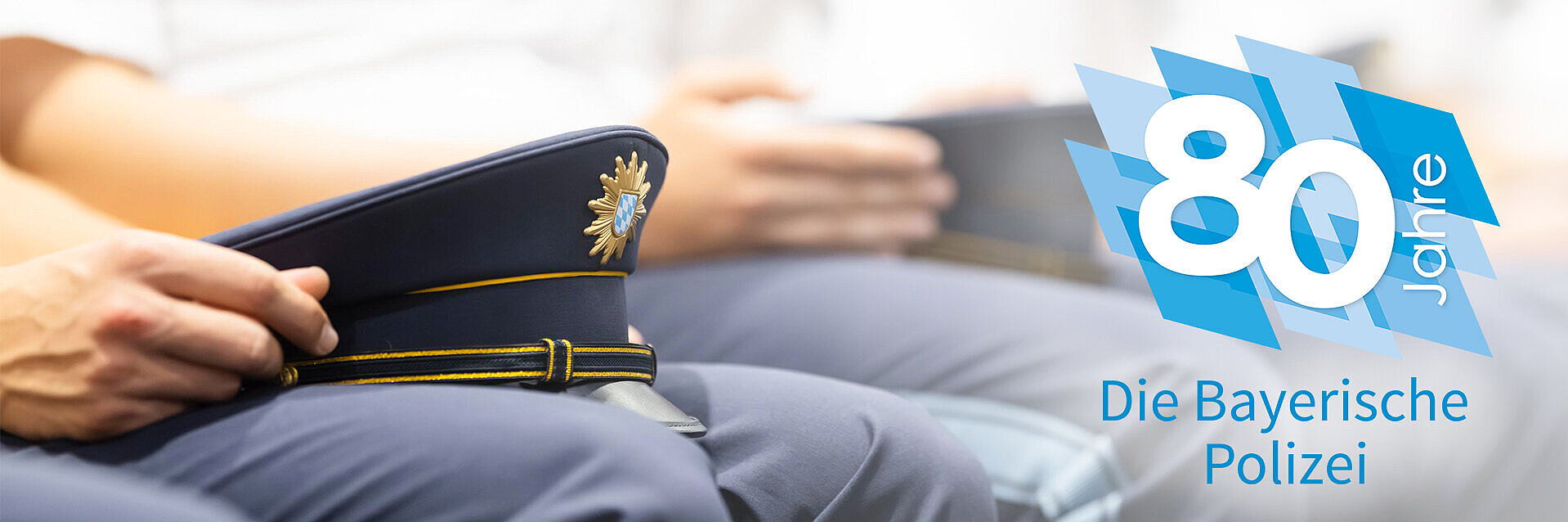 Polizeimütze mit bayerischem Wappen liegt auf dem Schoß zweier sitzender Personen; rechts großes blauer Schriftzug „80 Jahre – Die Bayerische Polizei“.