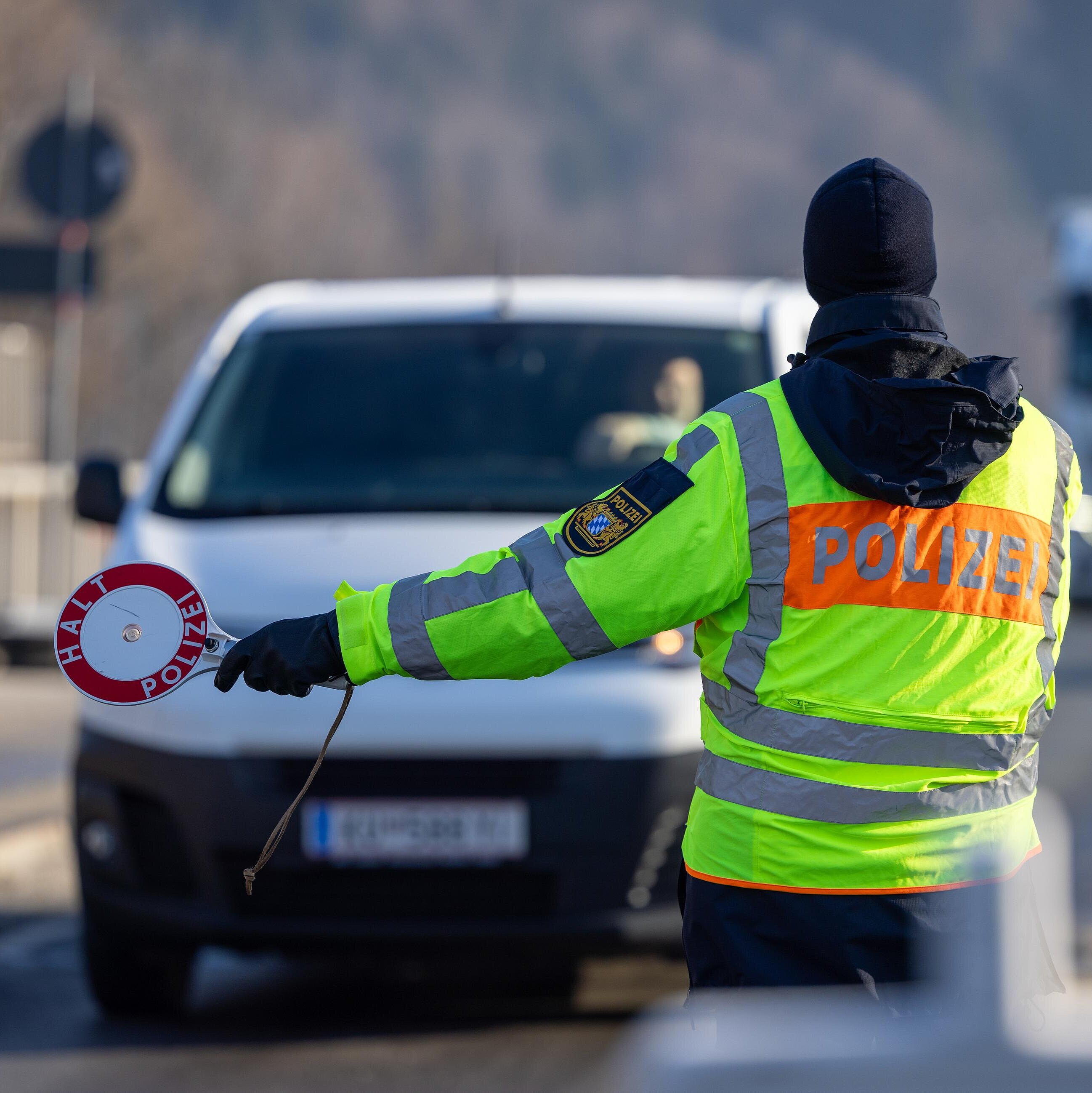 Polizist in Warnweste mit Polizeikelle stoppt einen weißen Van auf Straße