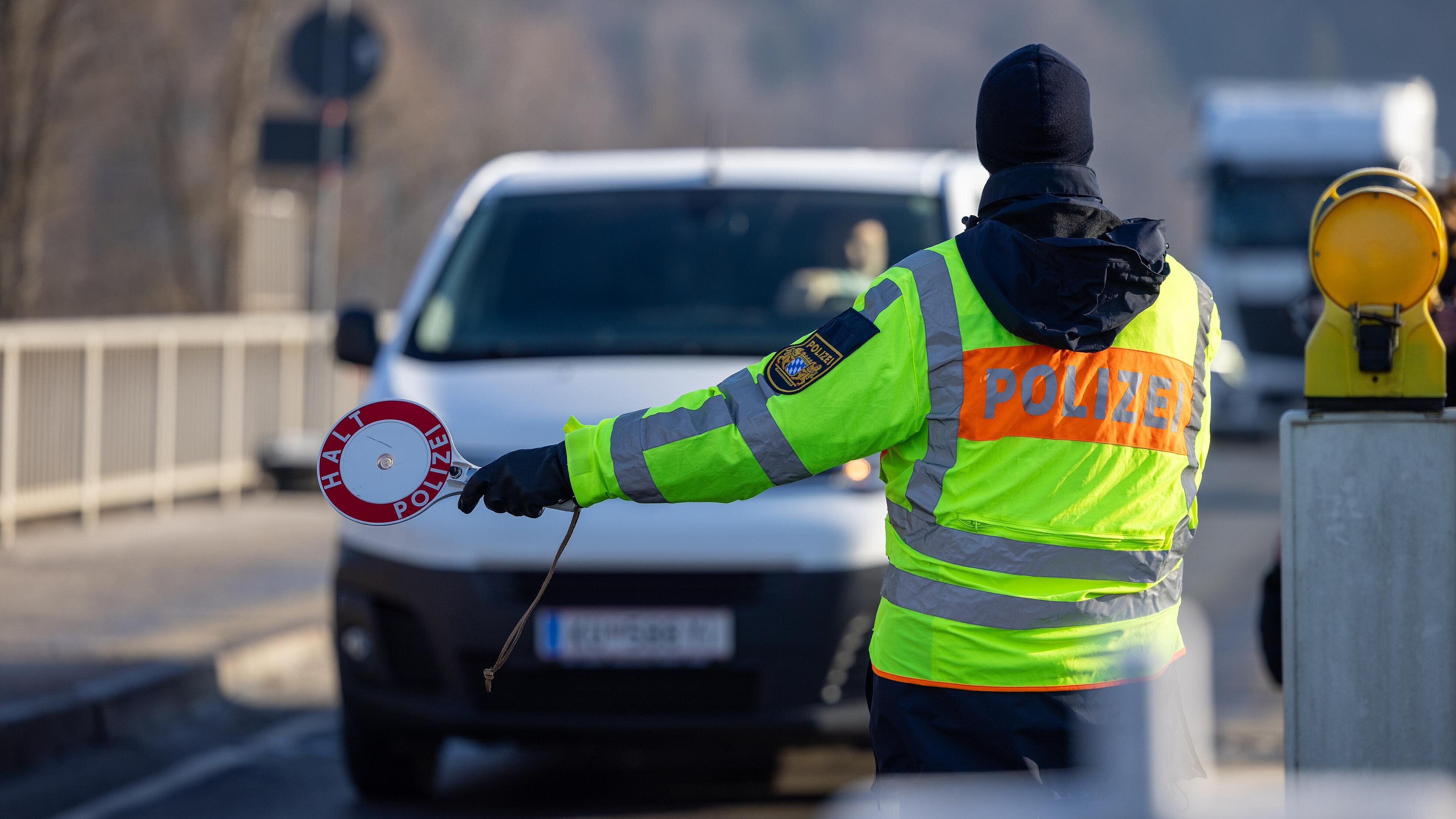 Polizist in Warnweste mit Polizeikelle stoppt einen weißen Van auf Straße