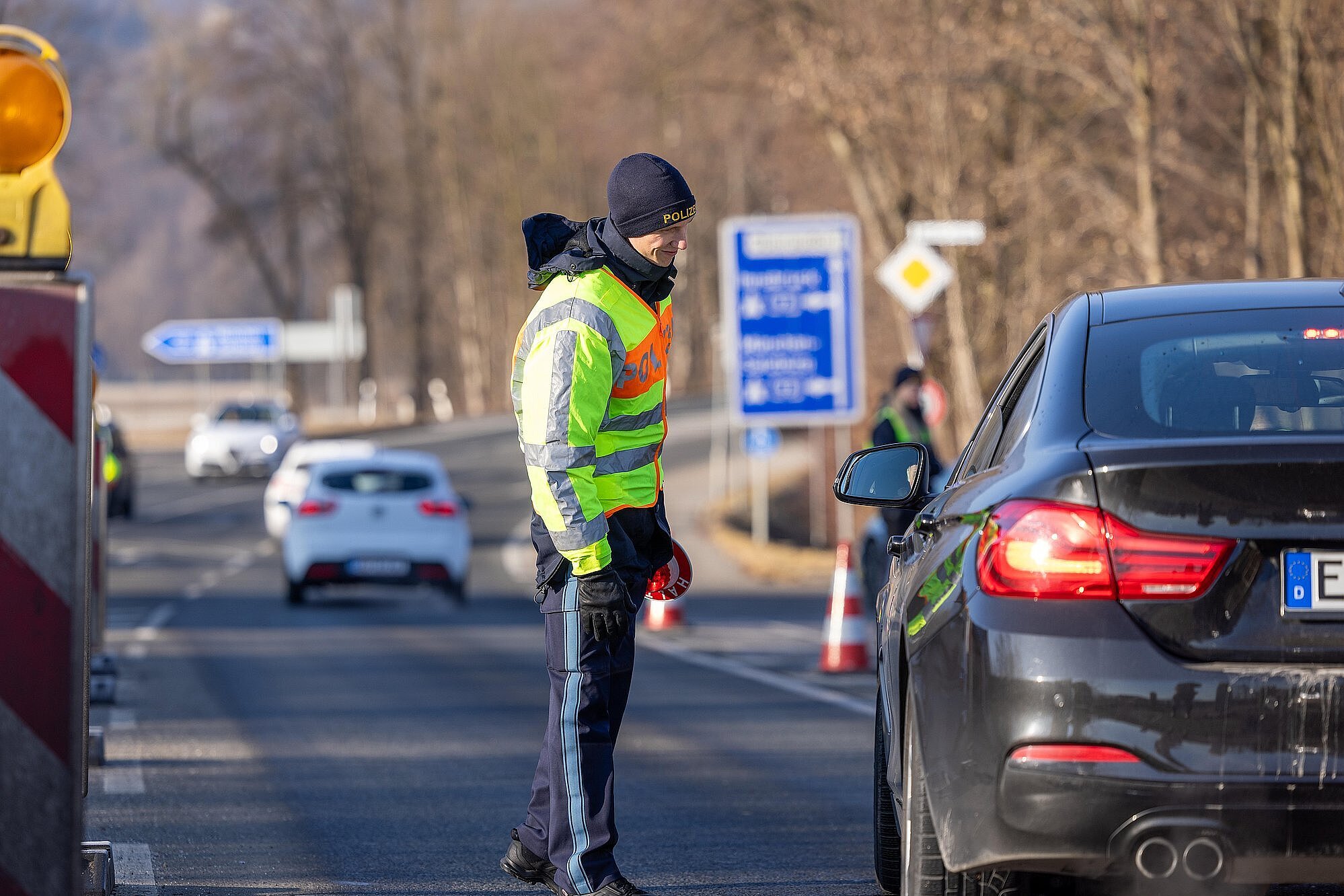 Ein Polizeibeamter mit Warnweste und Stoppkelle auf der Straße im Gespräch mit einem Autofahrer