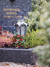 Grabstein mit einem Kerzenlicht und Blumen auf einem Friedhof