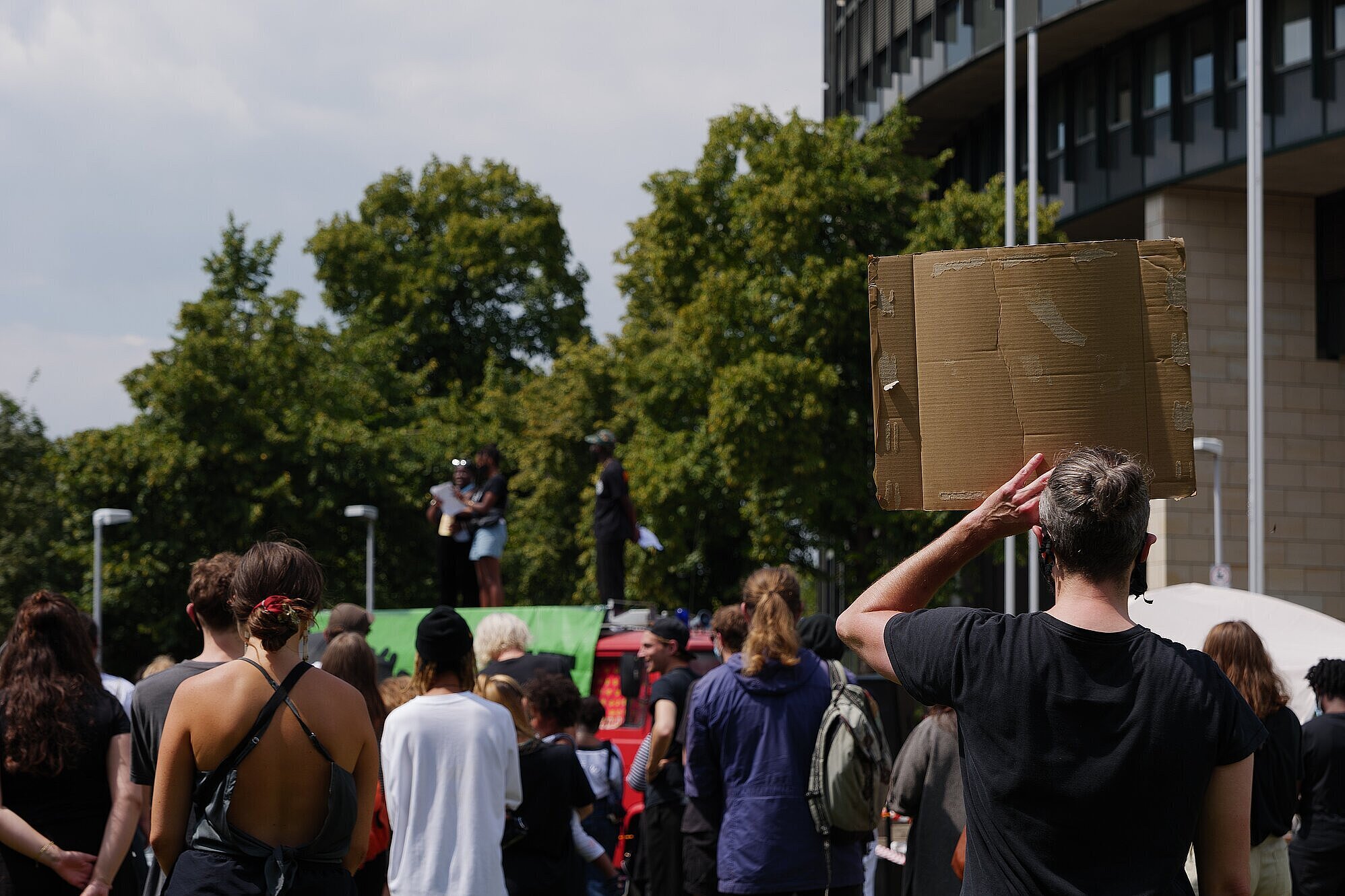 Menschenmenge, alle Personen sind von hinten abgebildet mit Blick auf eine Bühne, sie halten Schilder hoch 