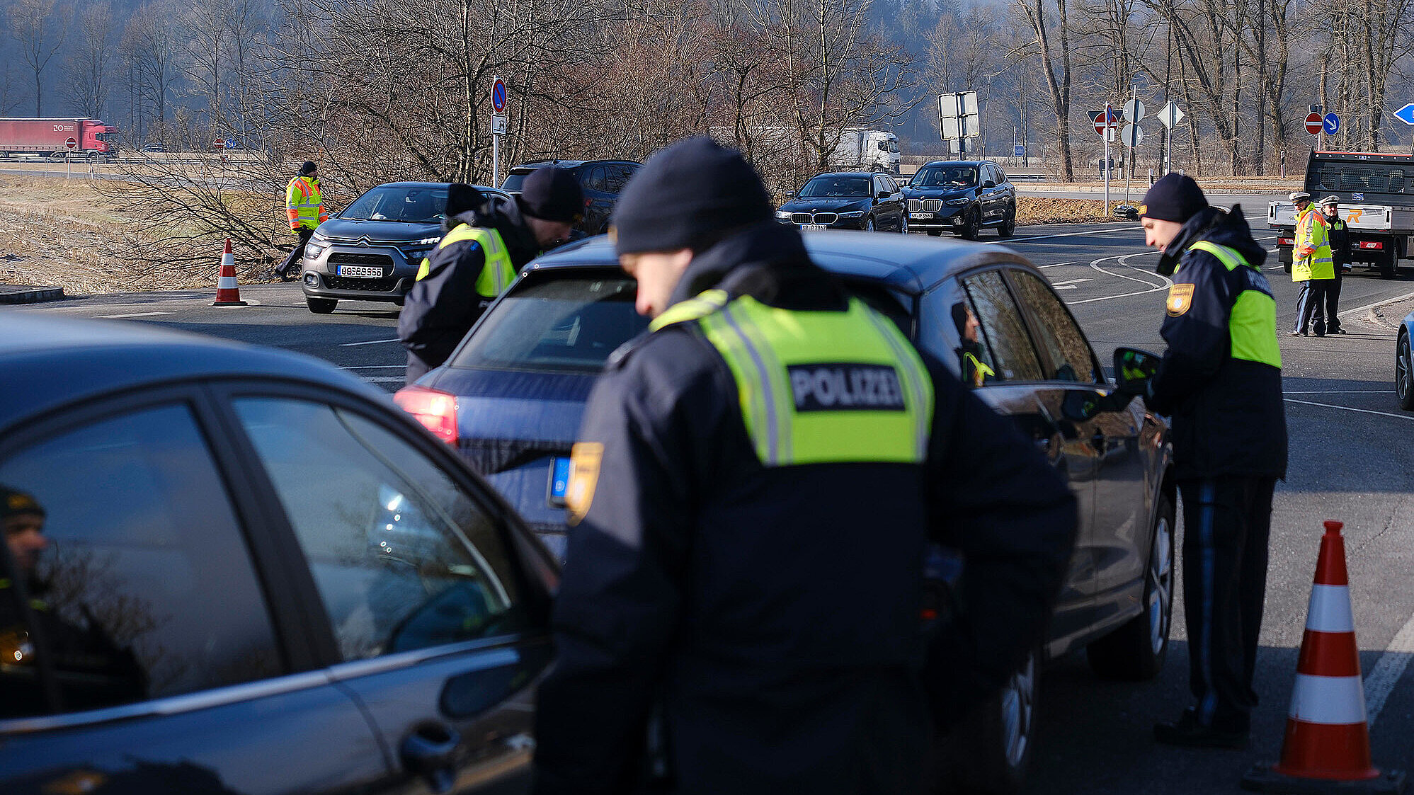 Polizisten kontrollieren mehrere Fahrzeuge bei einer Straßenkontrolle; Beamte in gelben Warnwesten sprechen mit den Fahrerinnen und Fahrern.