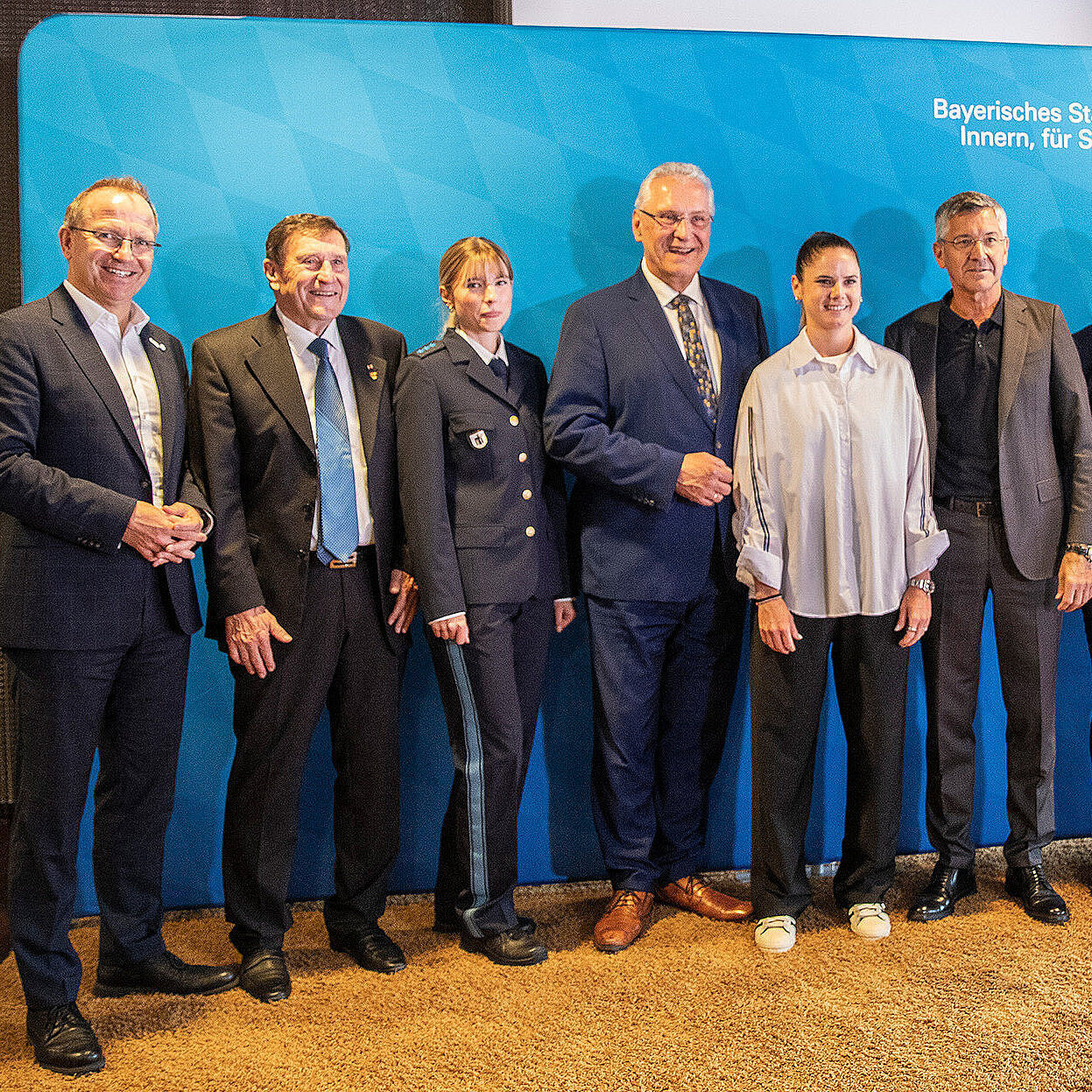 Gruppenbild anl. der Pressekonferenz Eure Fans in der Allianz Arena mit Innenminister Joachim Herrmann vor einer blauen Pressewand des StMI.