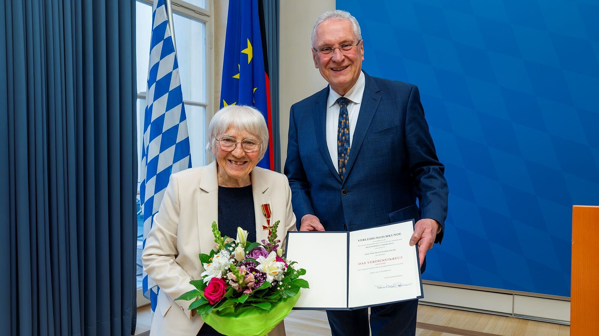 Waltraud Pfandlbauer mit Blumenstrauß und Innenminister Joachim Herrmann mit Urkunde lächeln den Fotografen an.