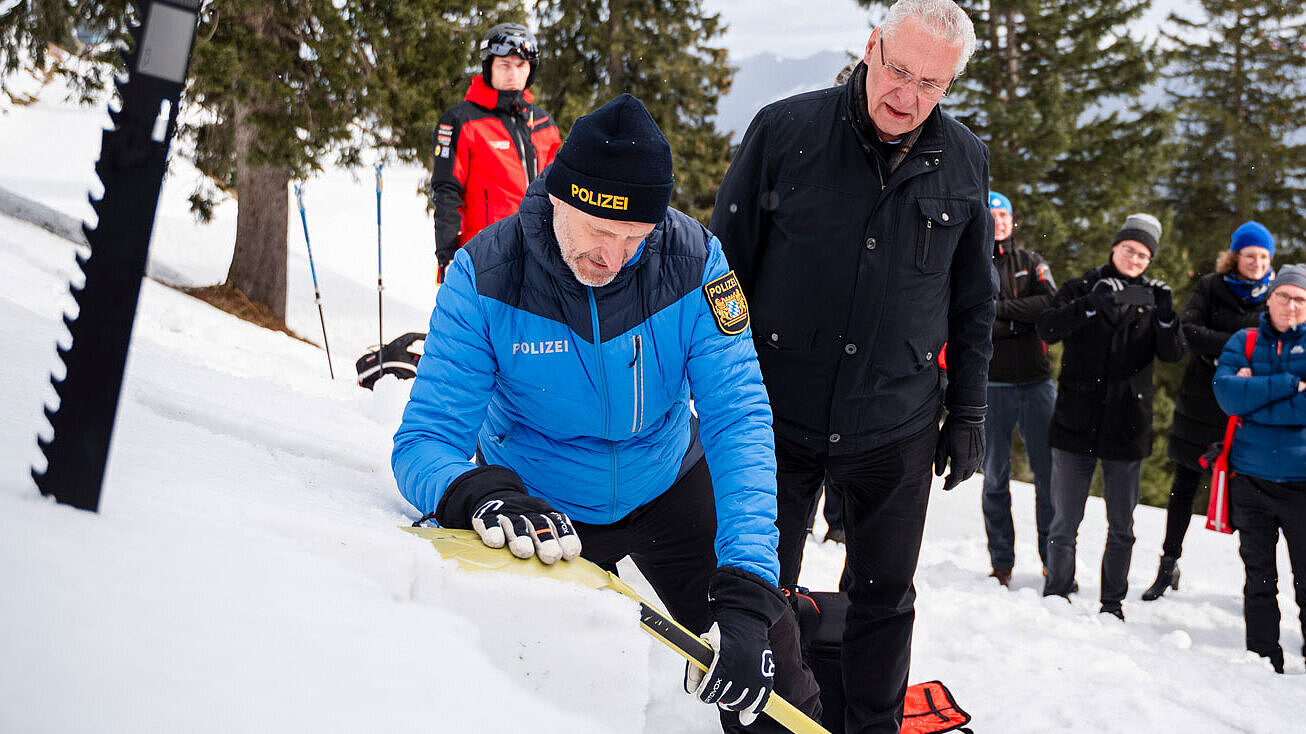 Innenminister Herrmann und Einsatzkräfte, u.a. ein Polizist, mit Lawinenschaufeln im Schnee
